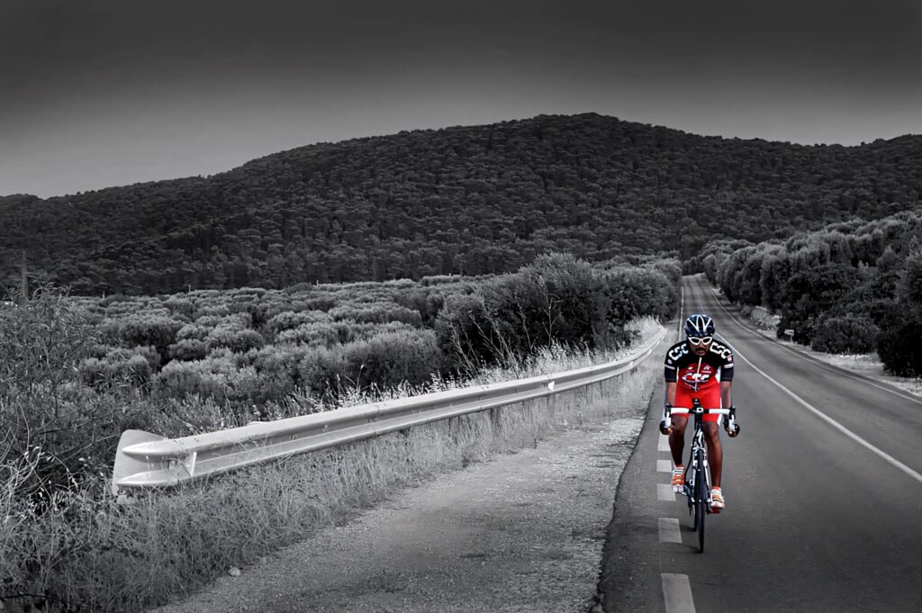 Solo cyclist in red gear riding on empty road through vast grayscale countryside landscape wallpaper background