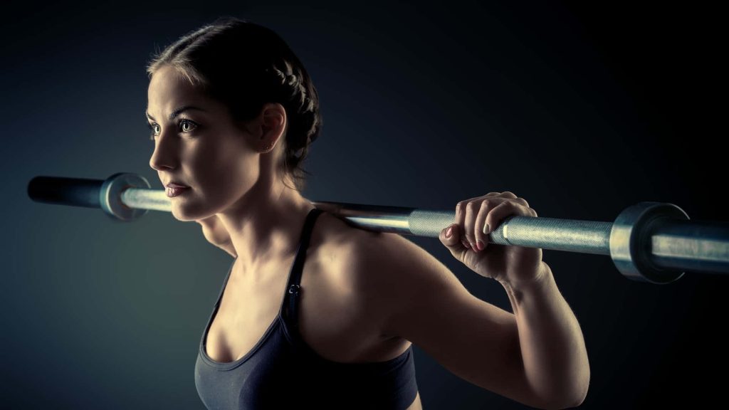 Determined woman doing barbell squat intense workout motivation dark minimalist background Wallpaper