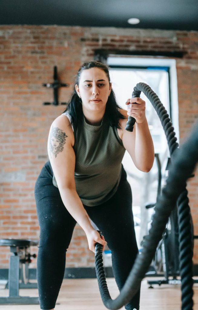 Determined woman doing battle rope workout in gym with rustic brick wall showing strength and focus Wallpaper