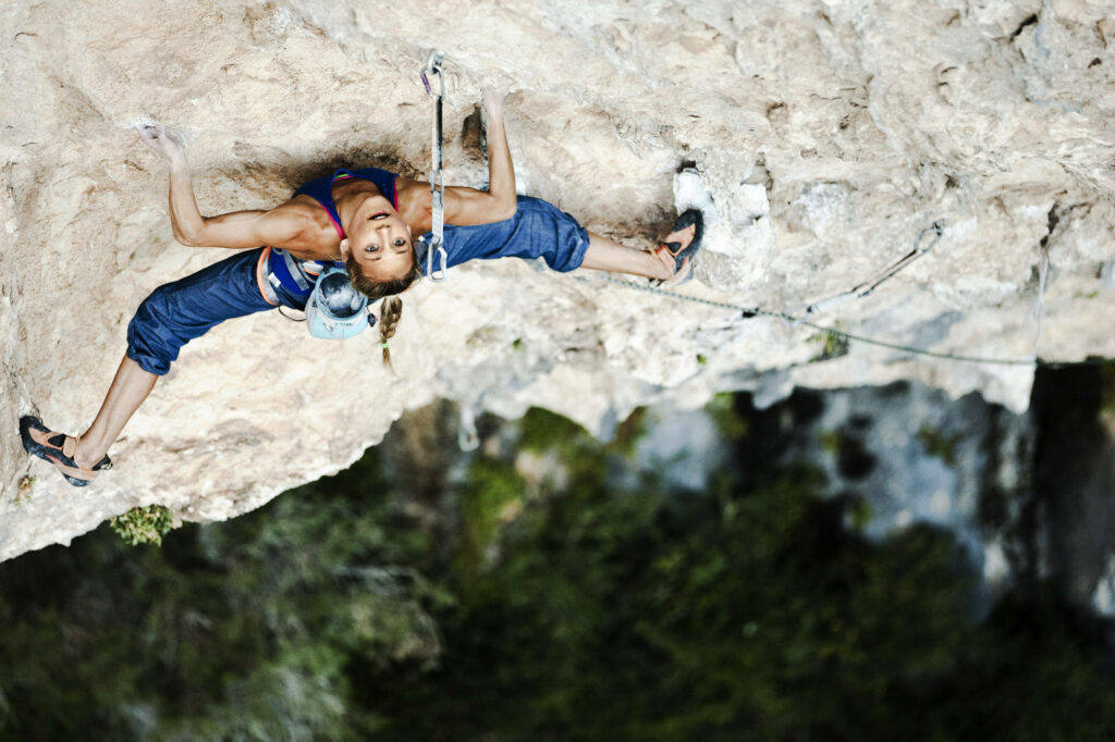 Determined woman rock climbing mid-ascent on rugged cliff with stunning natural scenery background Wallpaper