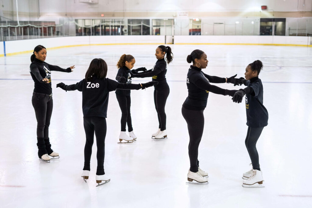 Young skaters from Detroit Figure Skating Club practicing together on bright indoor ice rink Wallpaper