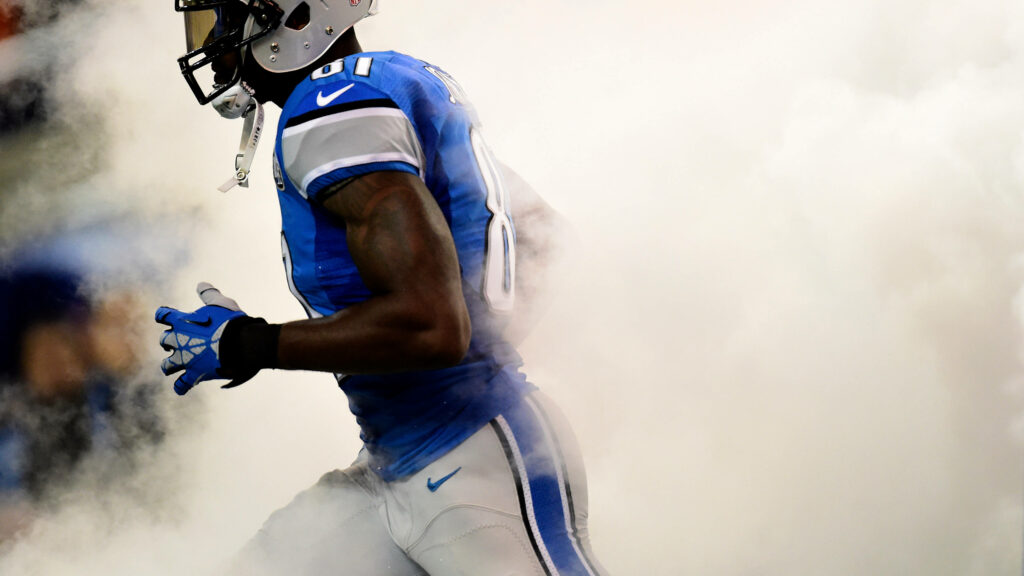 Detroit Lions player charges through smoky field in vivid blue and white game day action wallpaper