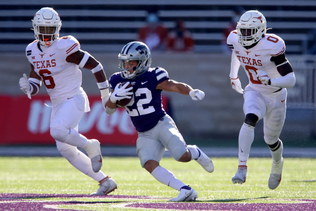 Deuce Vaughn evades Texas defenders displaying agility on a vibrant college football field action shot Wallpaper