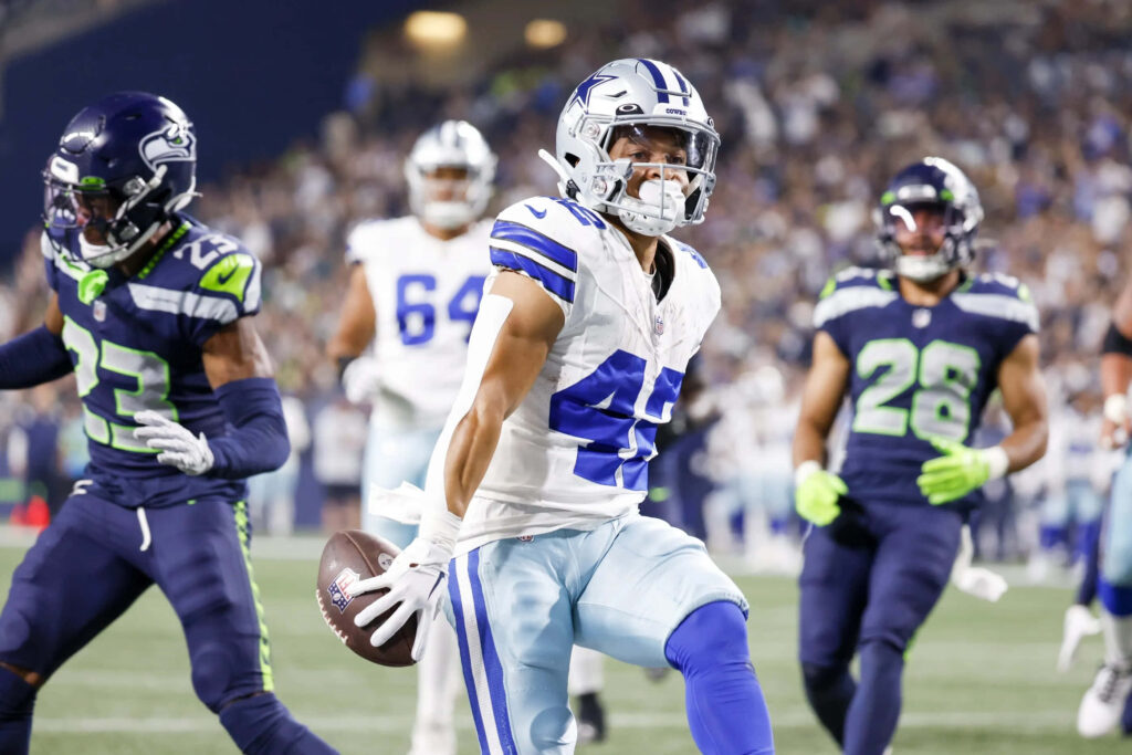 Deuce Vaughn sprinting in Dallas vs Seattle NFL game vibrant uniforms intense football action wallpaper