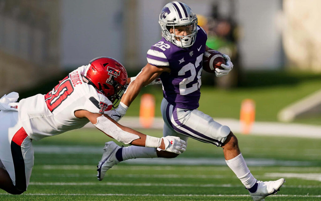 Deuce Vaughn Kansas State football evasive run dodging Texas Tech defender on sunlit field wallpaper
