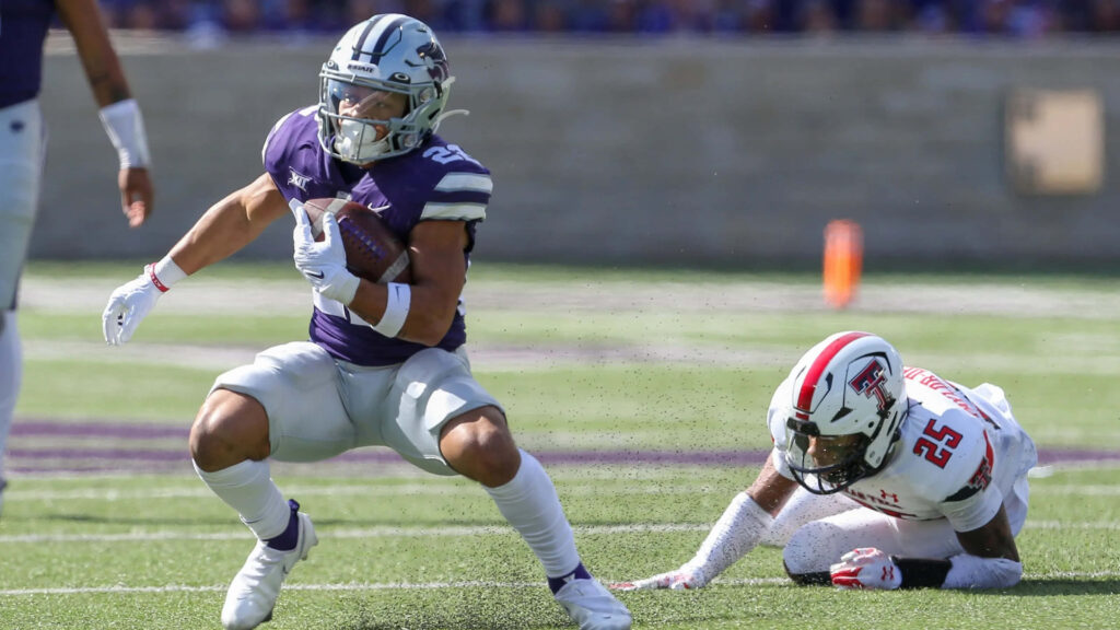 Deuce Vaughn in purple Kansas State uniform evades tackle showing agility in sunny football game Wallpaper