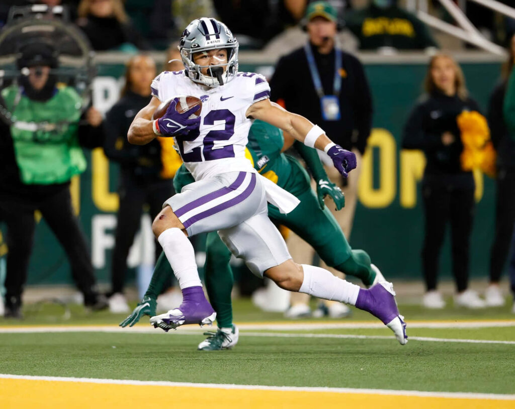 Deuce Vaughn Kansas State football sprinting action vibrant purple white uniform stadium background Wallpaper
