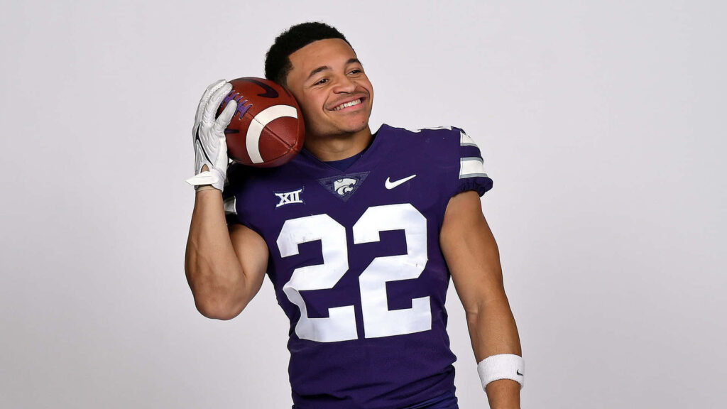 Deuce Vaughn smiling in Kansas State Wildcats number 22 uniform holding football studio photo Wallpaper
