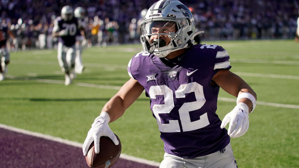 Deuce Vaughn sprinting in Kansas State football uniform on sunlit stadium field action shot Wallpaper