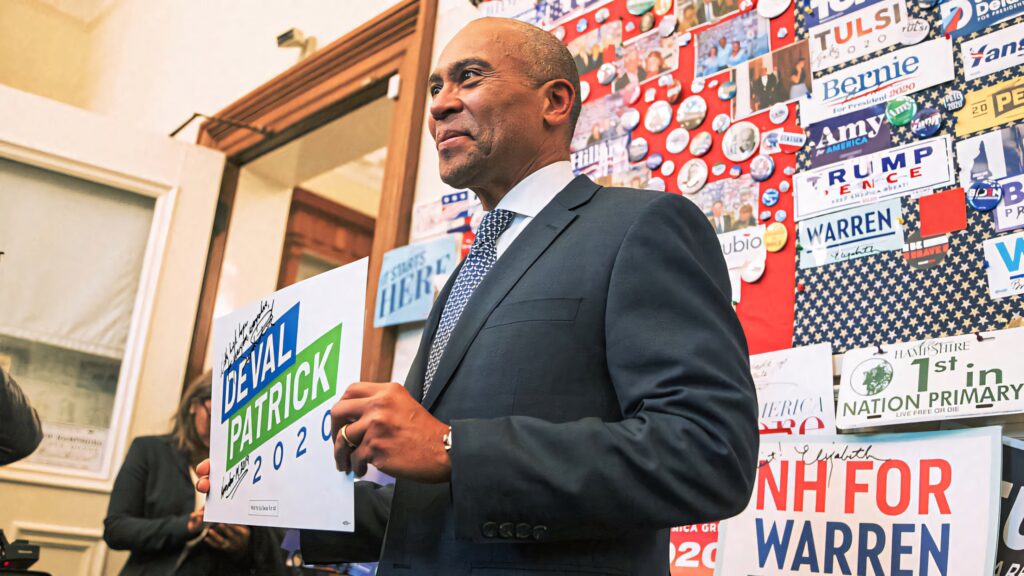 Deval Patrick speaking at vibrant 2020 campaign event with colorful political posters and buttons Wallpaper