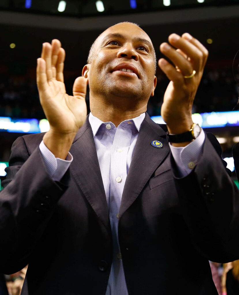 Deval Patrick clapping at event in dark suit with lively crowd and vibrant lighting background wallpaper