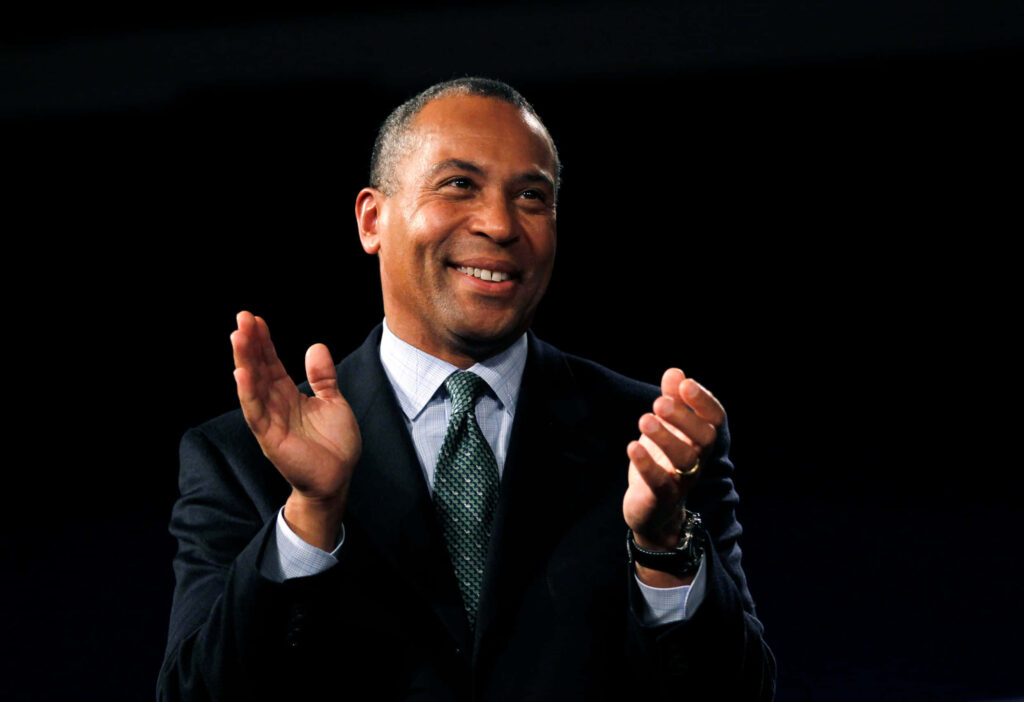 Deval Patrick clapping in dark suit and green tie with blurred dark background wallpaper