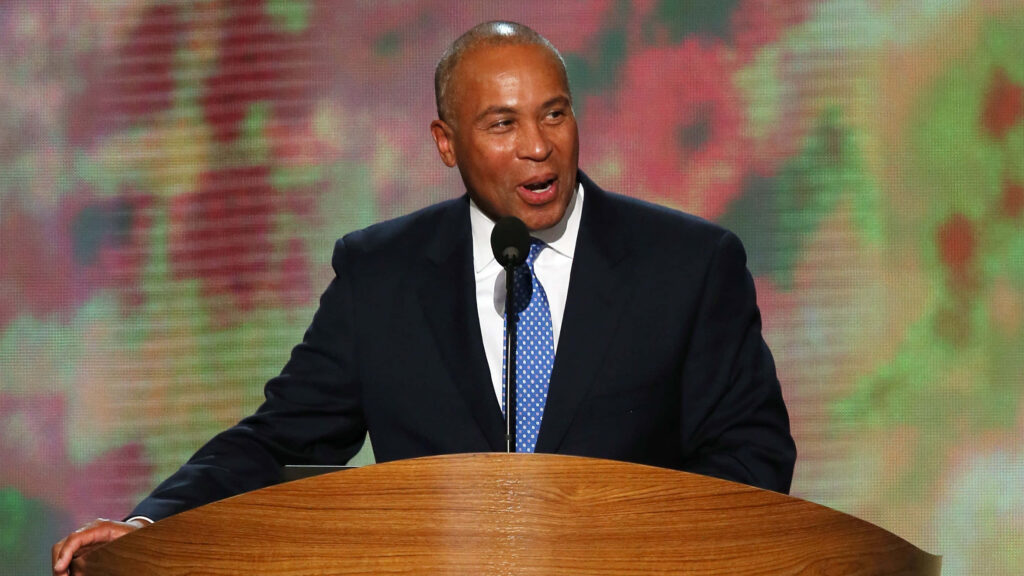 Deval Patrick speaking confidently at podium wearing dark suit and blue patterned tie vibrant background Wallpaper