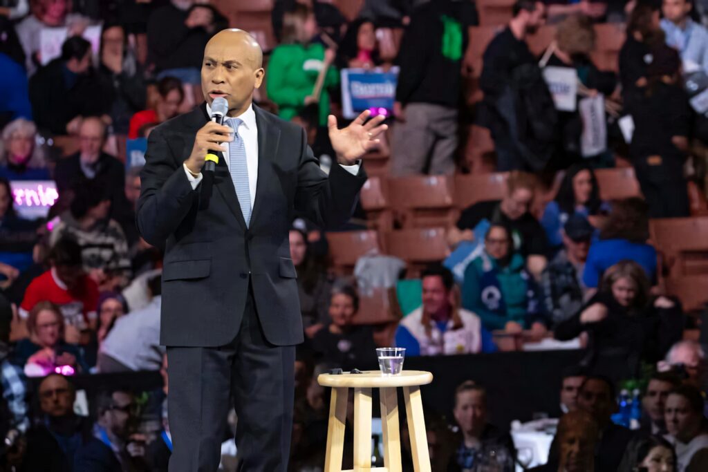 Deval Patrick speaking confidently in dark suit at lively public event with vibrant crowd background Wallpaper
