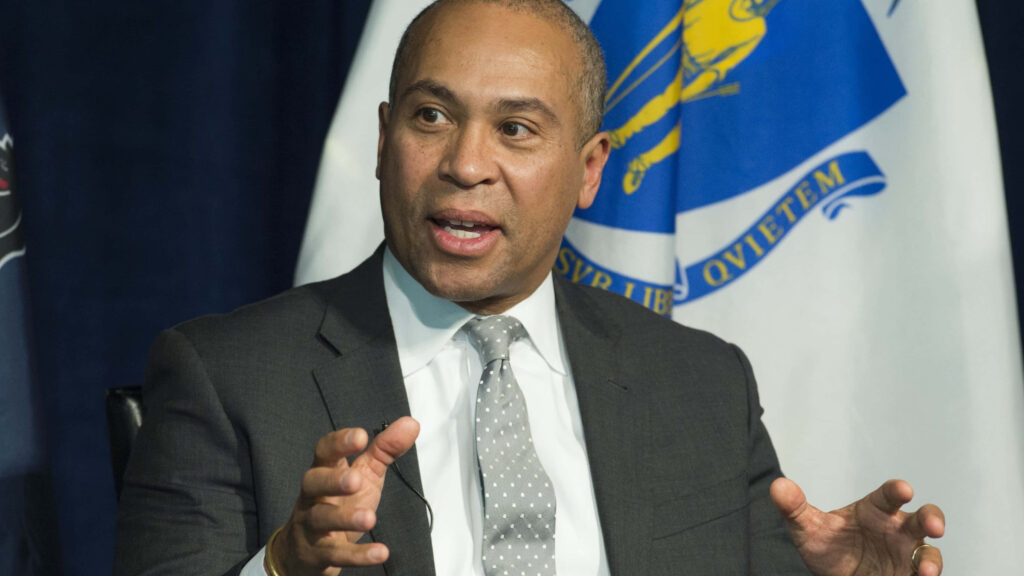 Deval Patrick in dark suit with polka-dot tie against official flags professional wallpaper background
