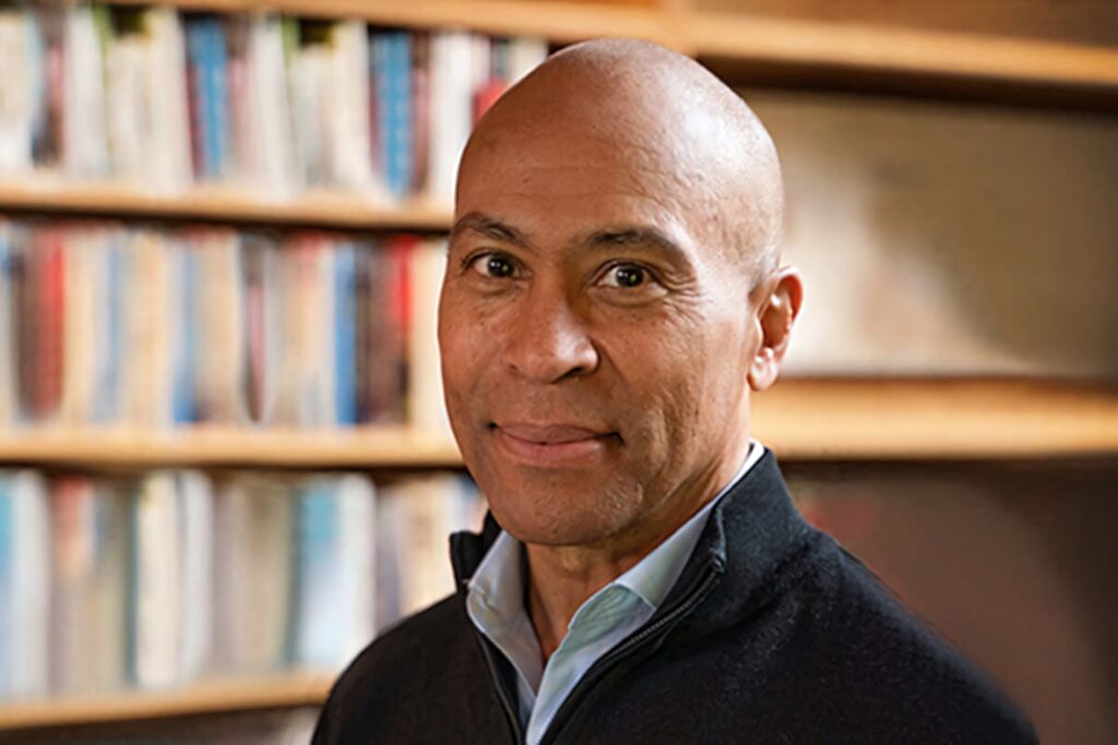 Deval Patrick smiling confidently in warm tones with blurred bookshelf background wallpaper