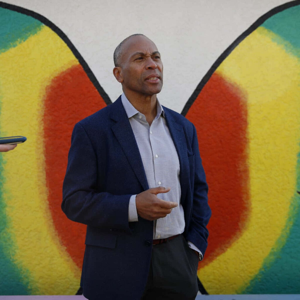 Deval Patrick in blue blazer stands focused against vibrant yellow green red mural background wallpaper