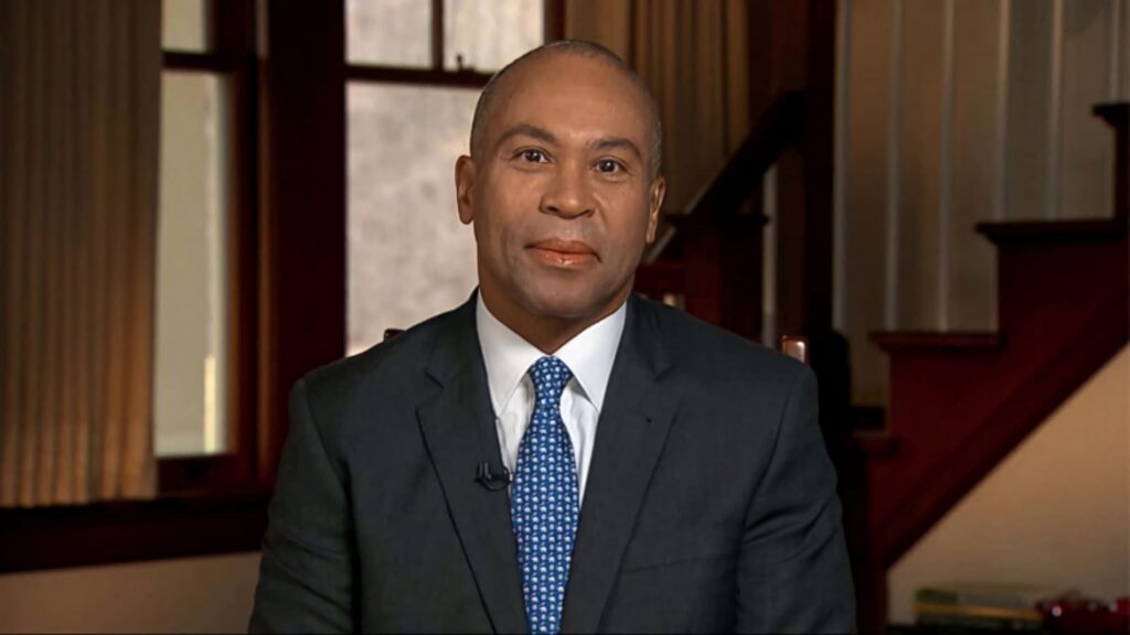 Former Governor Deval Patrick in formal suit seated by wooden staircase in elegant interior setting Wallpaper