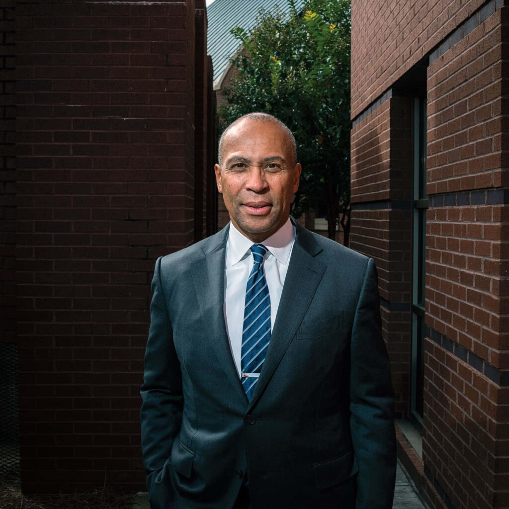 Deval Patrick in sharp suit and striped tie standing in brick alley with green trees background Wallpaper