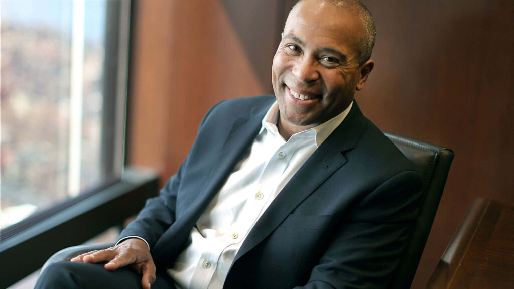 Deval Patrick in dark suit sitting by window in modern office with soft natural light background Wallpaper