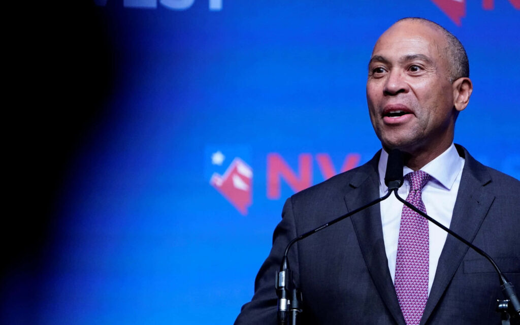 Deval Patrick speaking confidently at podium in dark suit against vibrant blue event backdrop Wallpaper