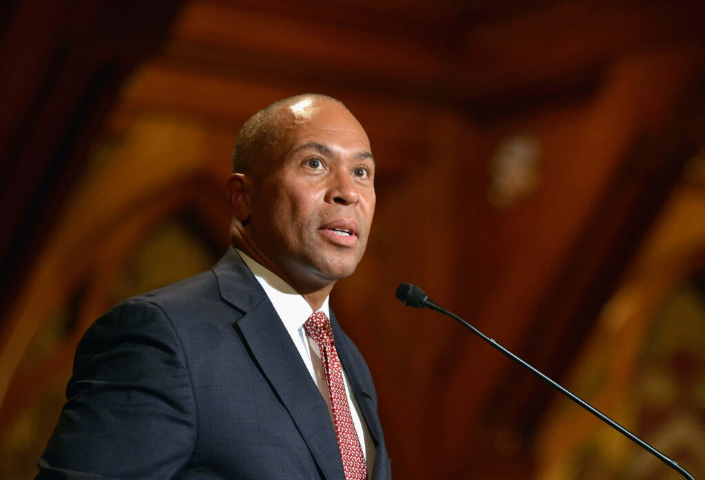 Deval Patrick speaking confidently at podium in formal setting with warm wood background lighting Wallpaper