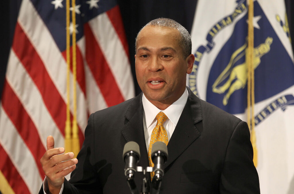 Deval Patrick speaking at official event with American and Massachusetts flags in background Wallpaper