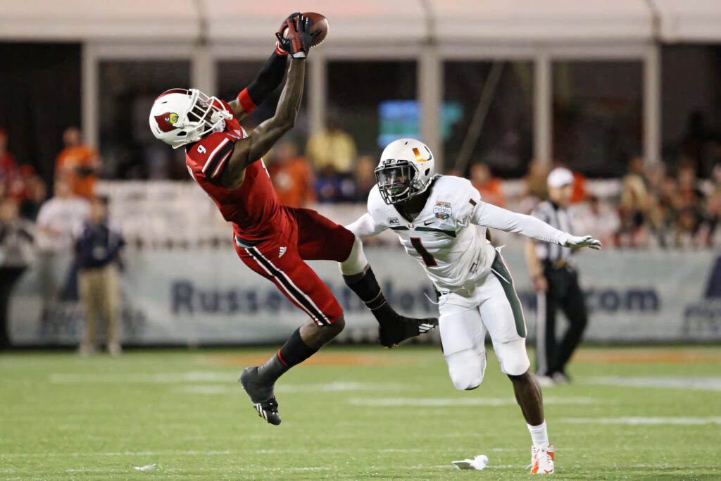 Devante Parker leaps high catching football in red white uniform on green field during intense game Wallpaper