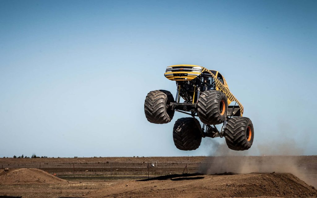 Yellow Devils monster truck jumping high over dirt track with blue sky background wallpaper