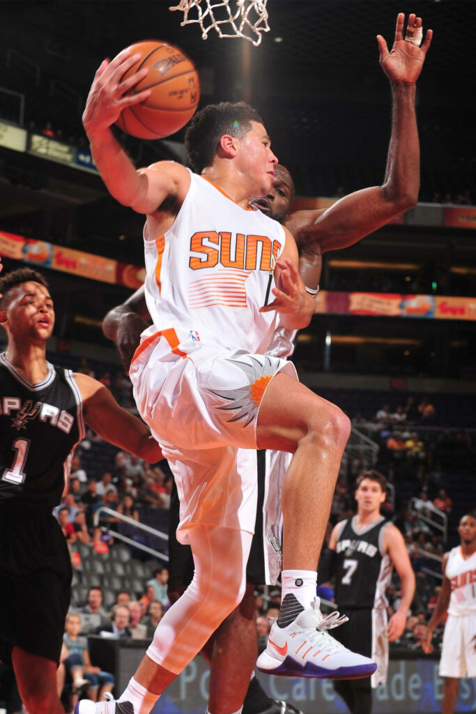 Devin Booker driving to basket vs Spurs center under bright arena lights NBA game action wallpaper