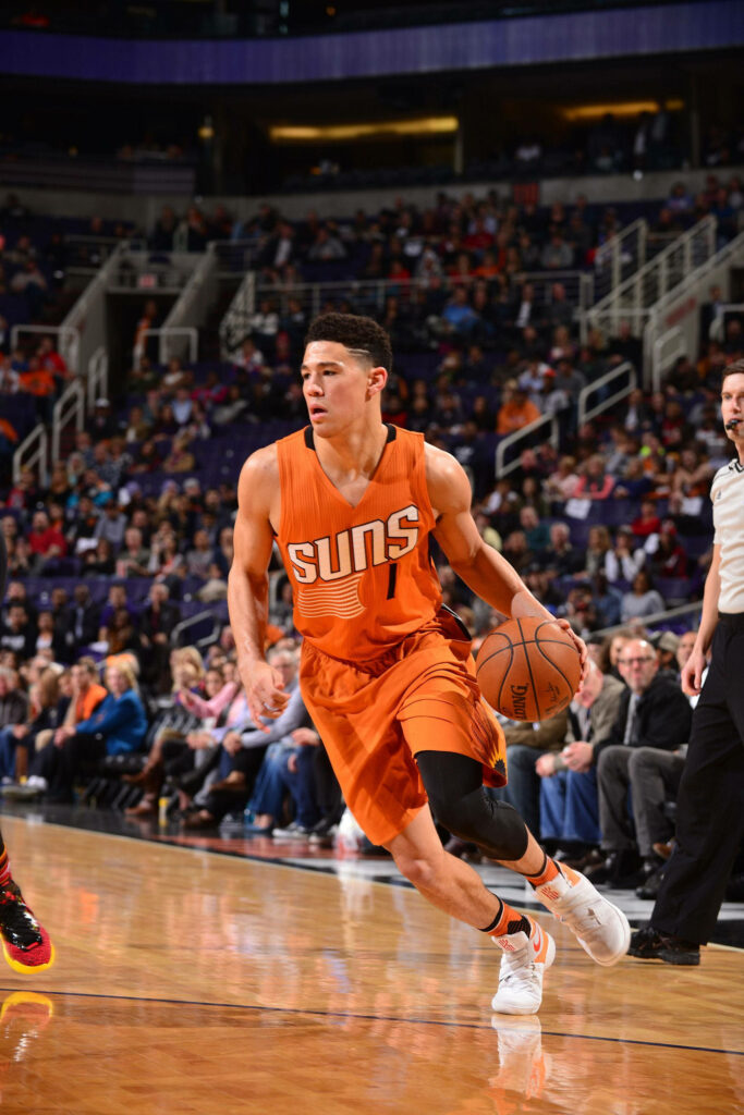 Devin Booker dribbling basketball in vibrant orange Suns uniform during intense game action Wallpaper