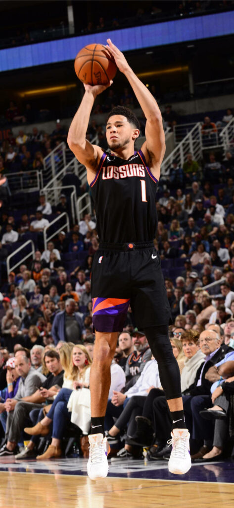 Devin Booker mid-jump shot in Los Suns black jersey with purple orange accents on court crowd background Wallpaper