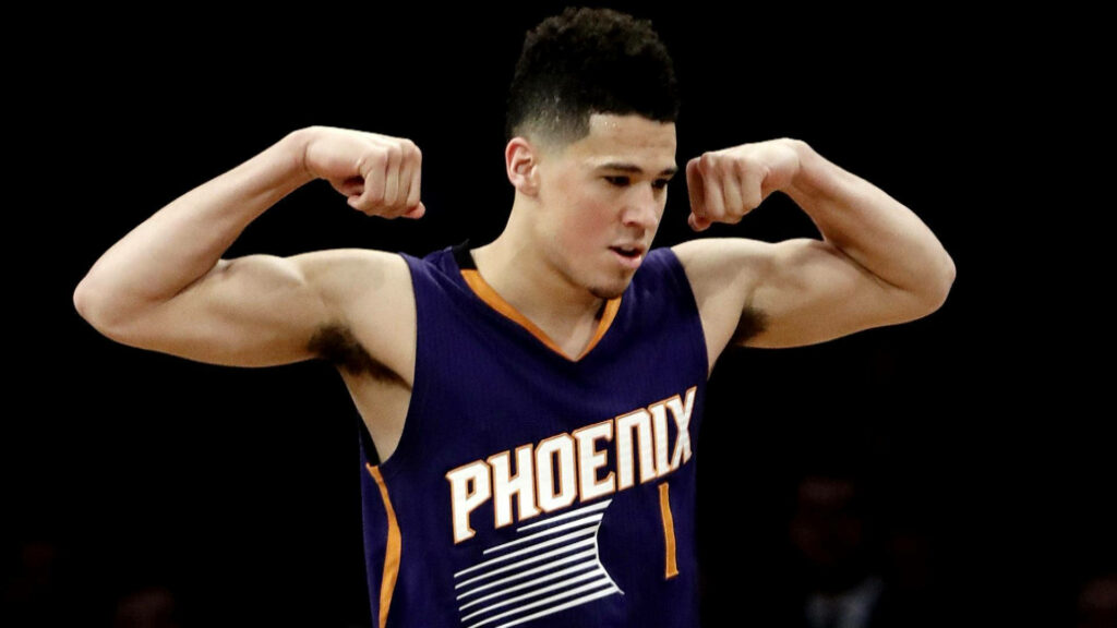 Devin Booker flexing muscles in Phoenix Suns jersey showcasing strength and determination wallpaper