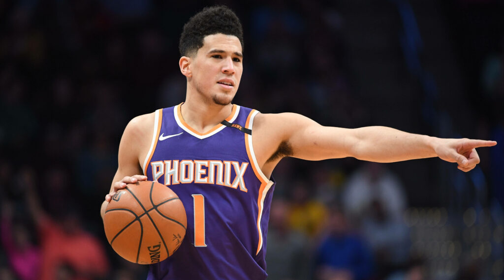Devin Booker focused on court pointing in Phoenix Suns jersey showcasing leadership and intensity Wallpaper