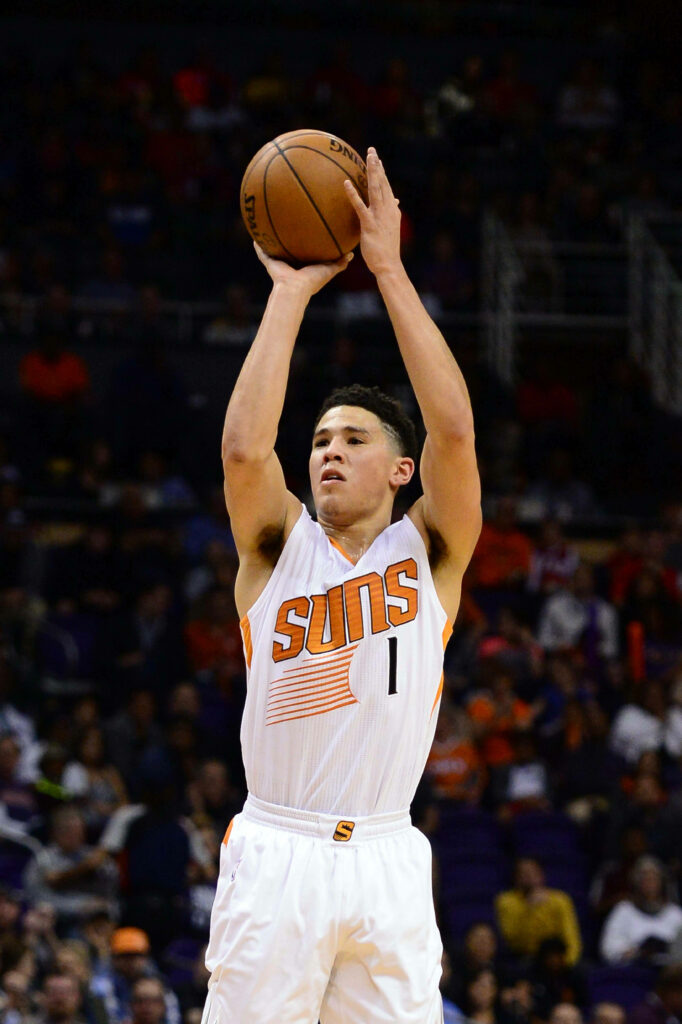 Devin Booker shooting in Phoenix Suns white uniform intense gameplay action blurred arena background Wallpaper