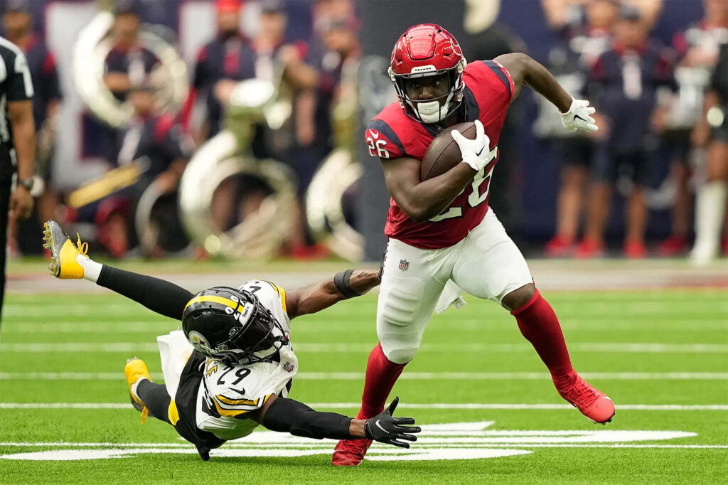 Devin Singletary sprinting on green football field in red uniform evading tackle with intense focus Wallpaper