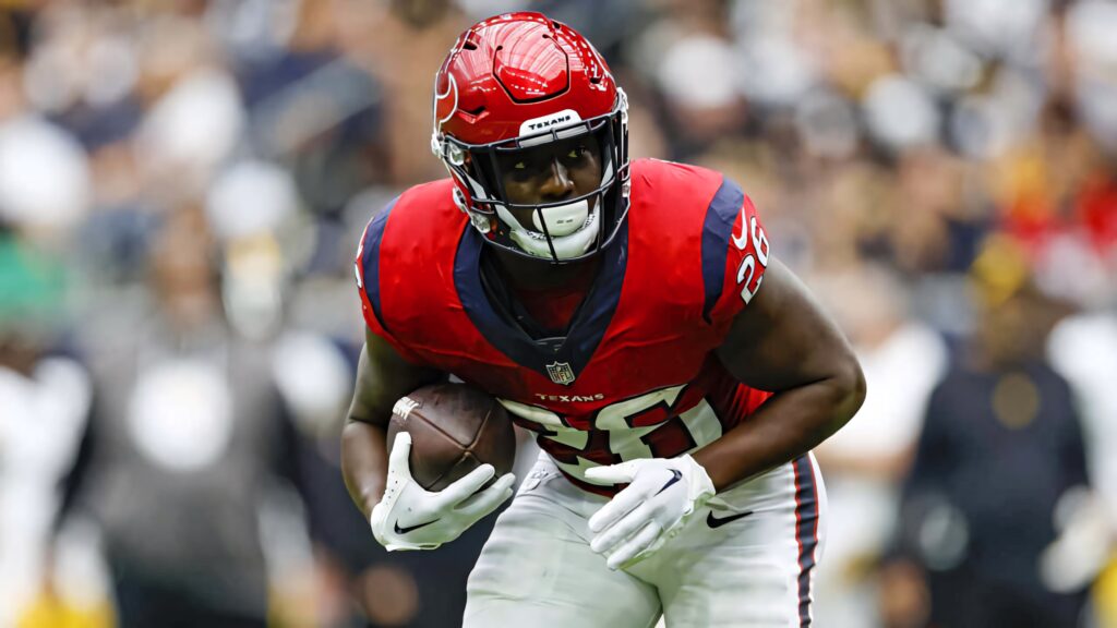 Devin Singletary in red Houston Texans uniform clutching football during intense game play Wallpaper