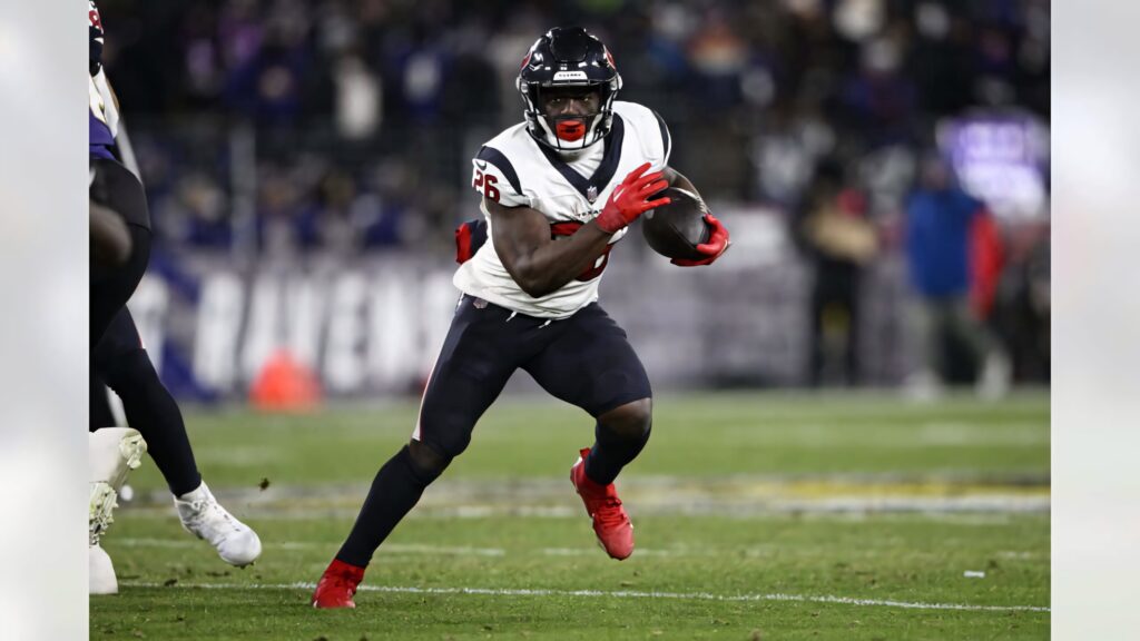 Devin Singletary in Houston Texans uniform with red gloves and cleats charging in intense game Wallpaper