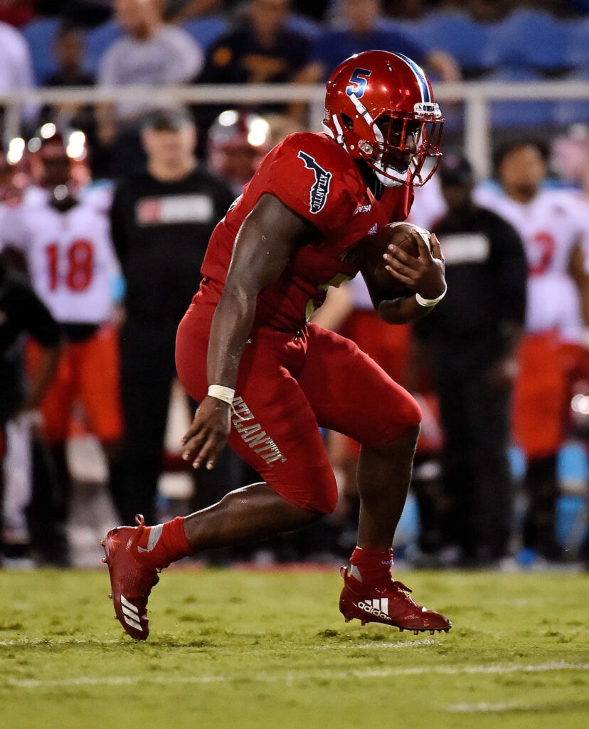 Devin Singletary running with football in red uniform on vibrant field with stadium lights Wallpaper
