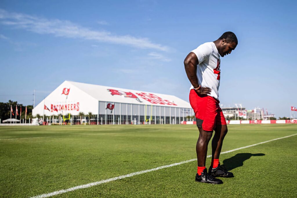 Devin White focused on Buccaneers training camp field wearing team gear under branded tent Wallpaper