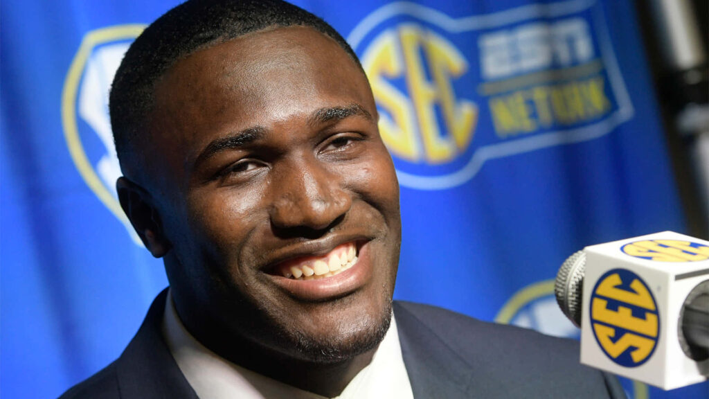 Devin White smiling confidently in dark suit at SEC Network press conference with blue backdrop Wallpaper