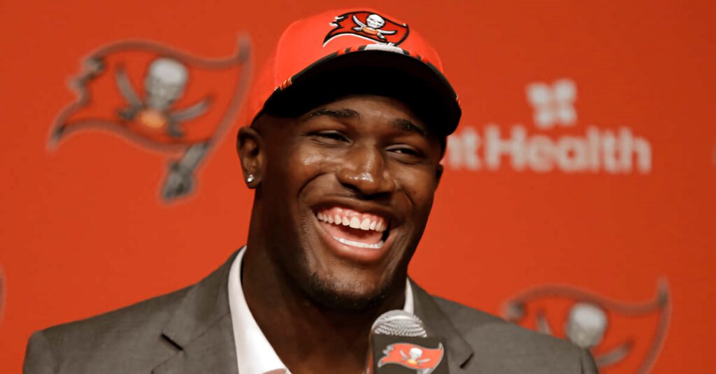 Devin White smiling in Tampa Bay Buccaneers cap and suit at vibrant red team press conference background Wallpaper
