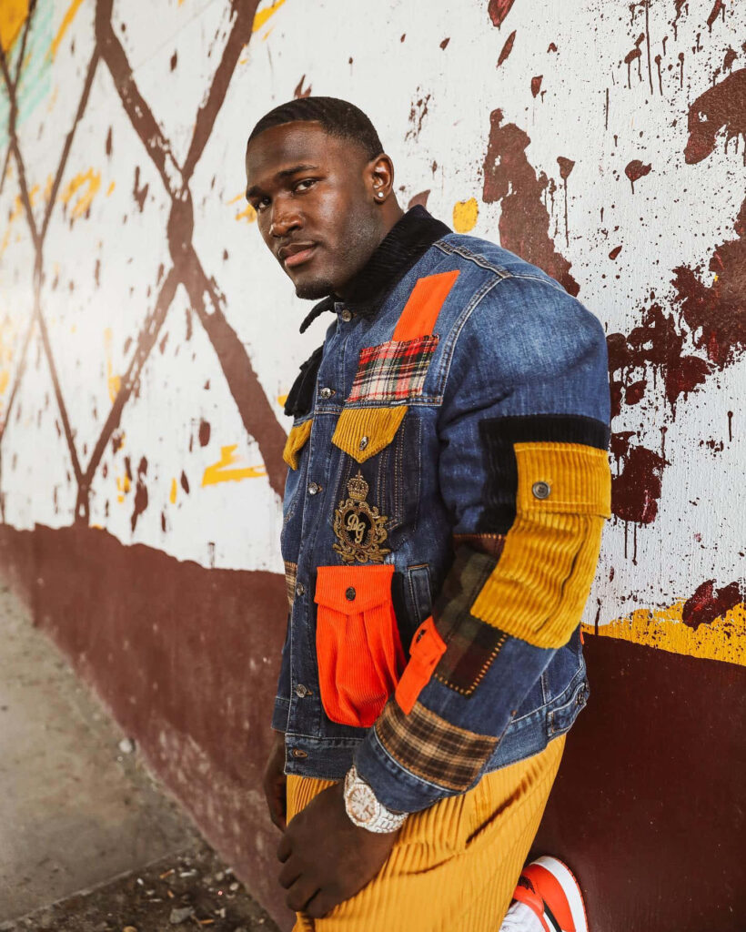 Devin White in stylish denim jacket and yellow pants standing by bold urban street art wall Wallpaper