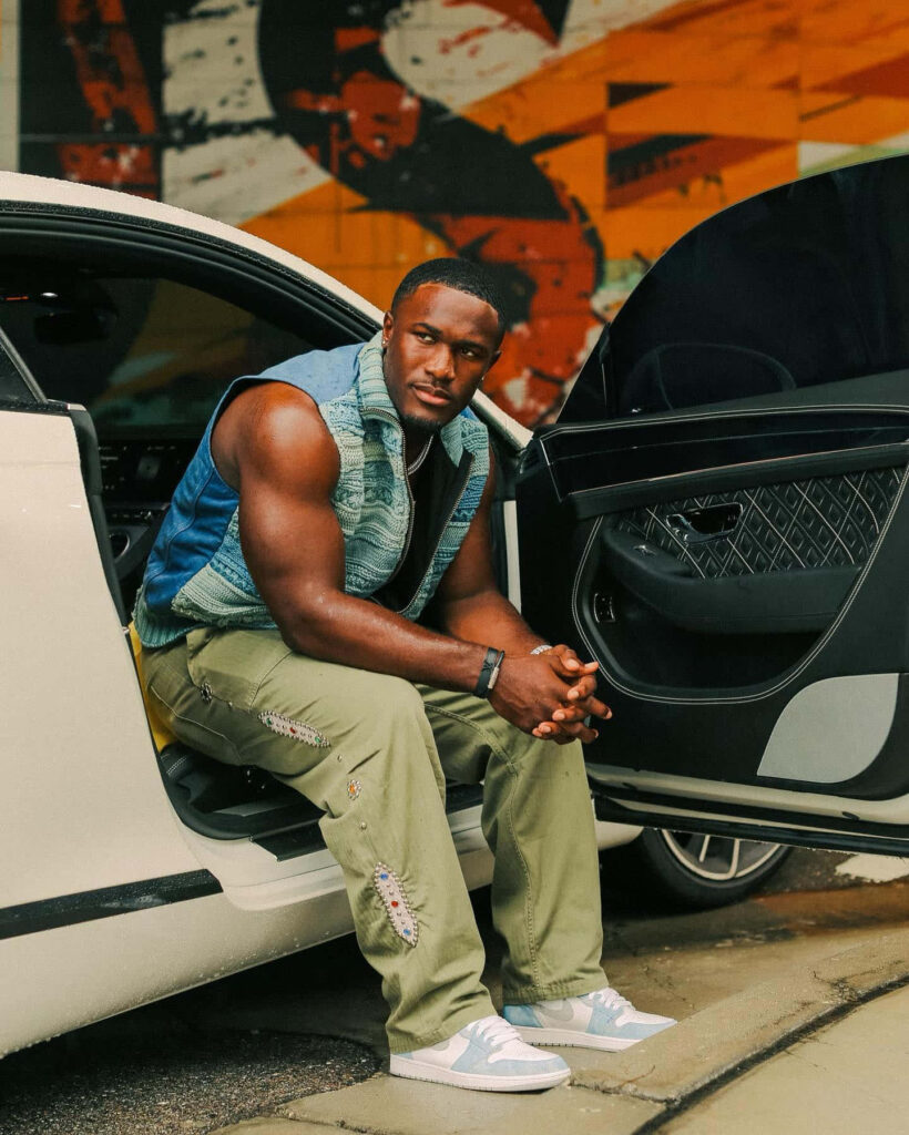 Devin White in denim vest and khaki pants by white car with vibrant urban mural background Wallpaper
