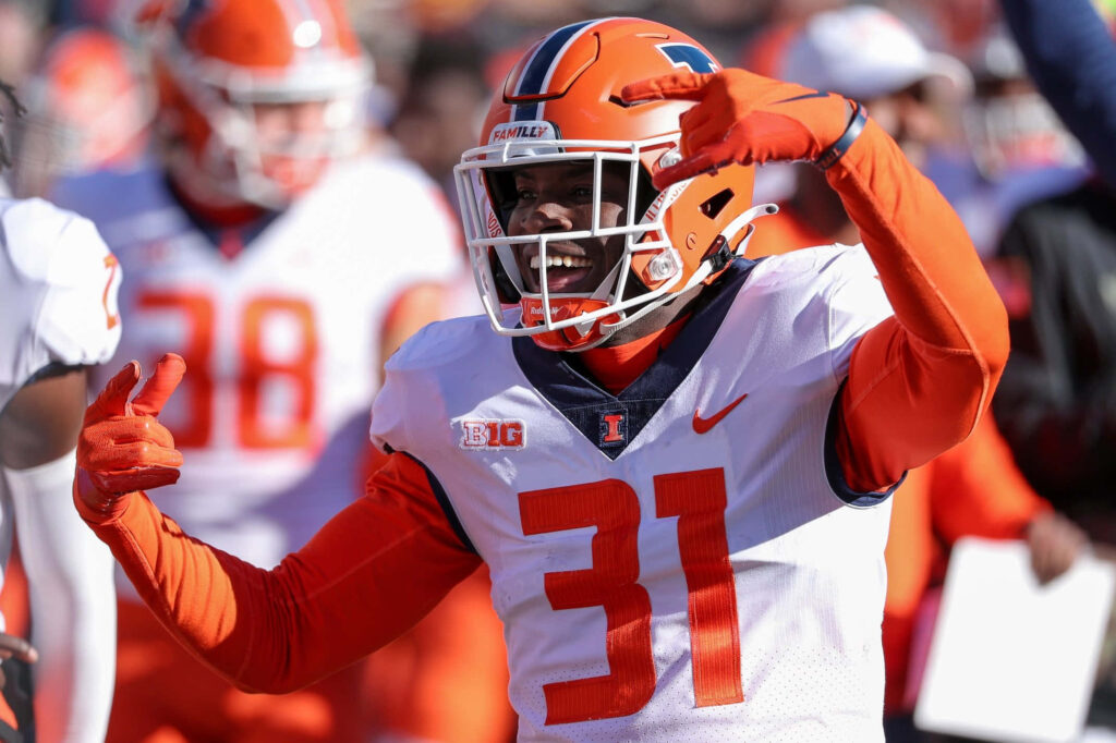 Illinois Football player Devon Witherspoon celebrating on field vibrant orange white uniform action Wallpaper