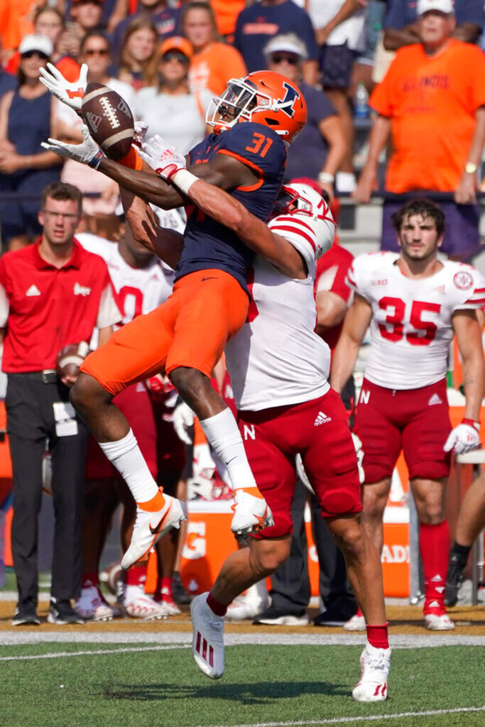 Devon Witherspoon leaps mid-air for a football catch battling tight coverage in vibrant game action Wallpaper
