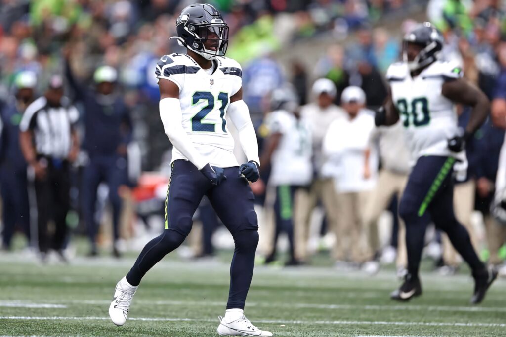 Devon Witherspoon in Seattle Seahawks number 21 uniform stands focused on vibrant football field during game Wallpaper