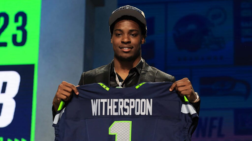 Devon Witherspoon holds Seattle Seahawks jersey on NFL Draft Day blue green background wallpaper