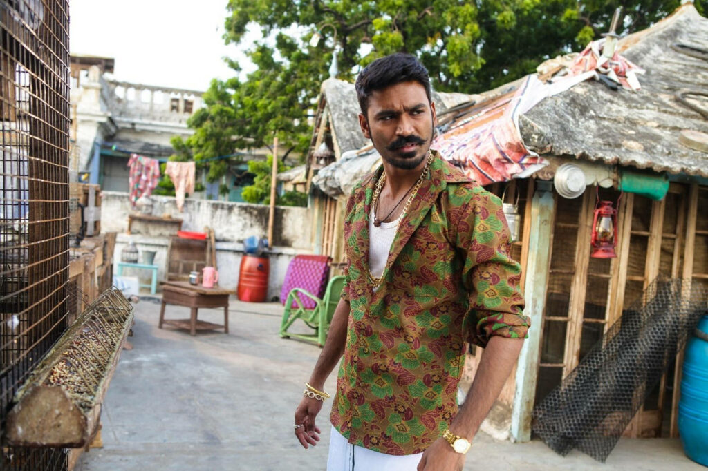 Dhanush in patterned shirt and gold accessories in vibrant rustic urban backdrop with natural light Wallpaper