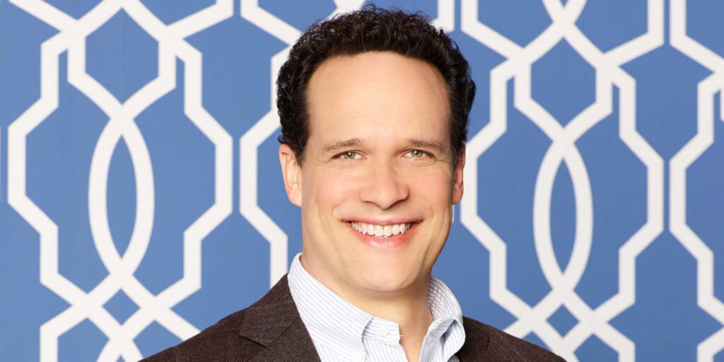 Diedrich Bader smiling portrait with geometric blue white pattern modern vibrant wallpaper